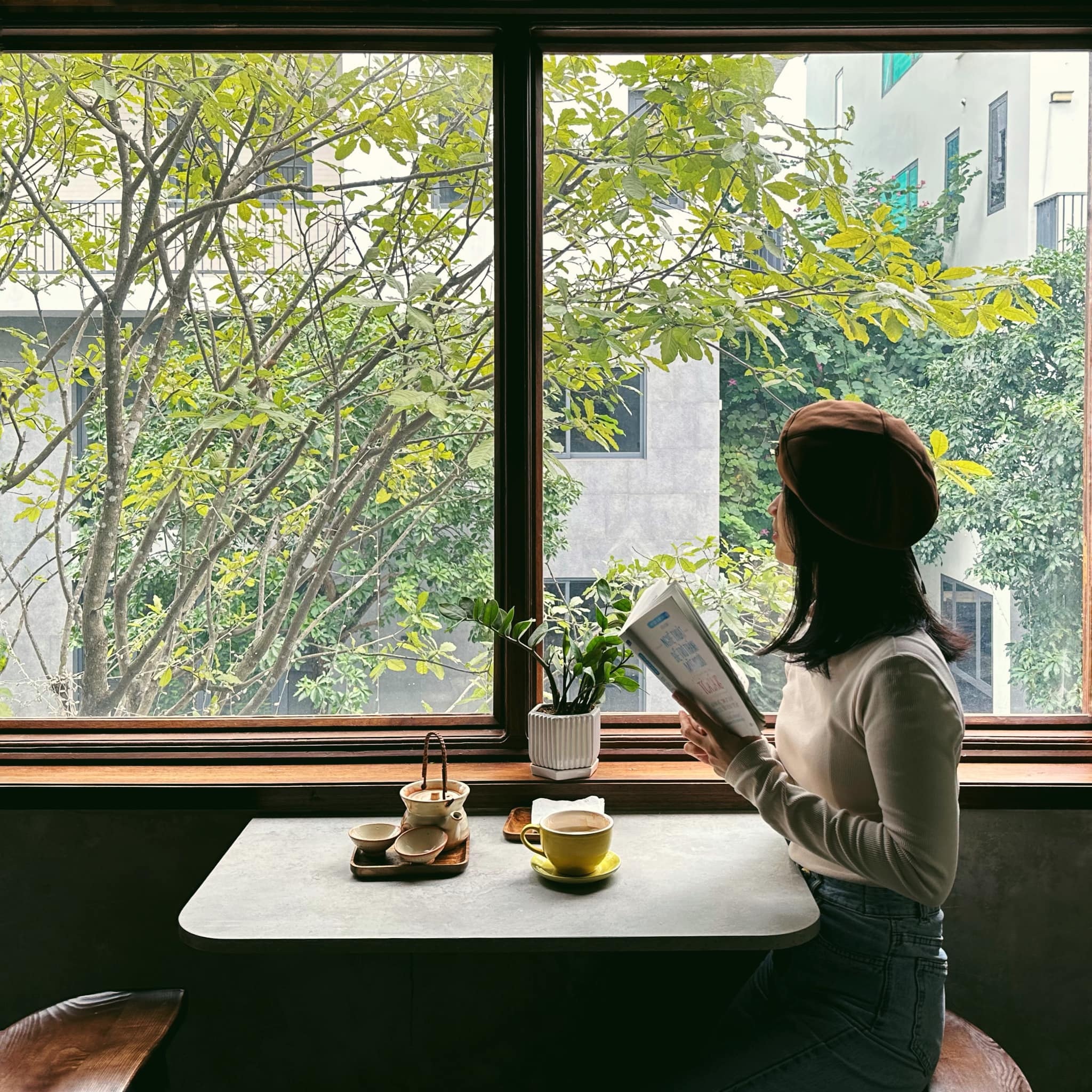 Người phụ nữ đọc sách trên ban công với tách trà